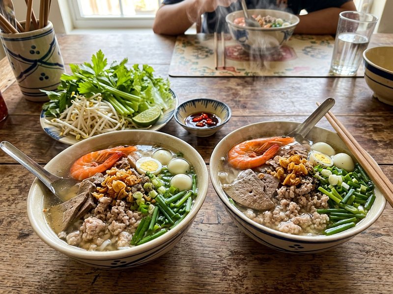 Hai tô hủ tiếu Nam Vang đầy đặn topping tôm thịt gan trứng cút tỏi phi bên đĩa rau sống giá hẹ cần tây