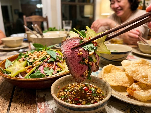 Đôi đũa gắp miếng thịt bò mềm mọng kèm khế sao chấm chén nước mắm ớt cay
